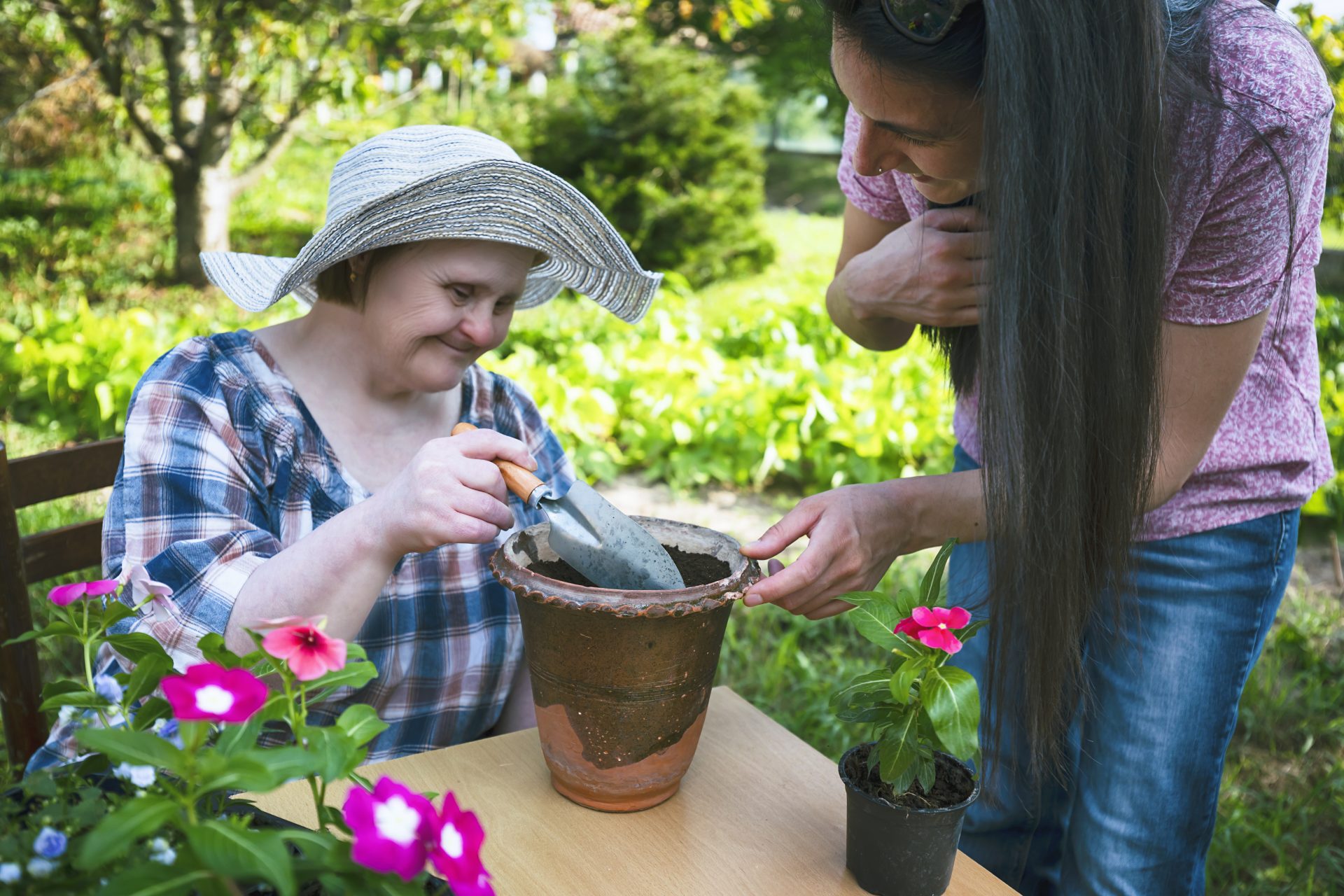 Woman with Down Syndrome and her friend planting flowers together. Gardening.