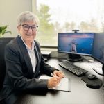 woman wearing black jacket and sitting at desk with pen in hand