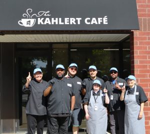 Group of 7 people wearing chef aprons and hats in front of cafe