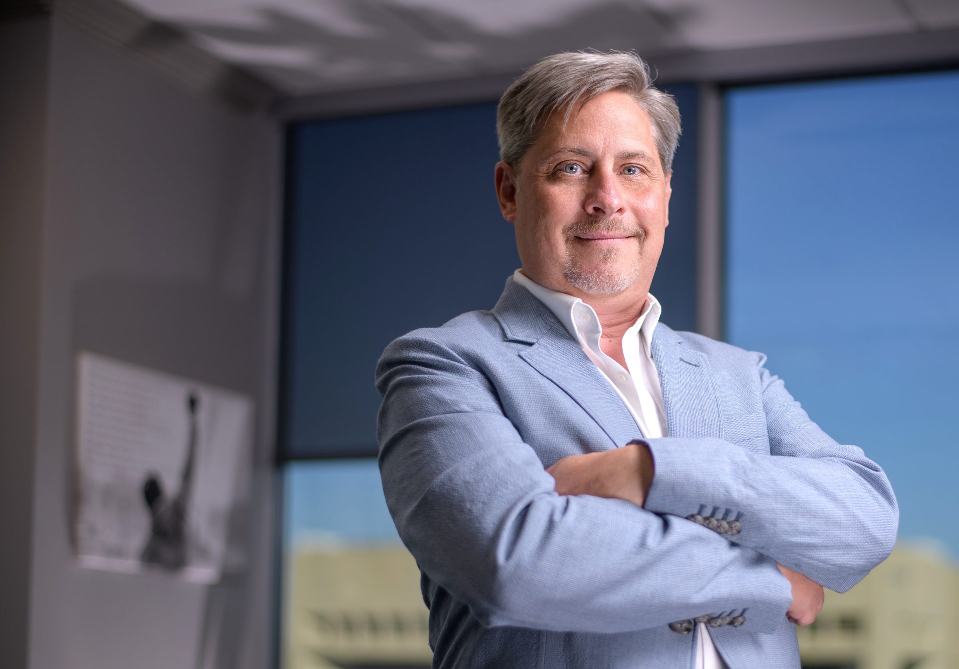 Businessman wearing blue sport coat standing with arms crossed in executive office